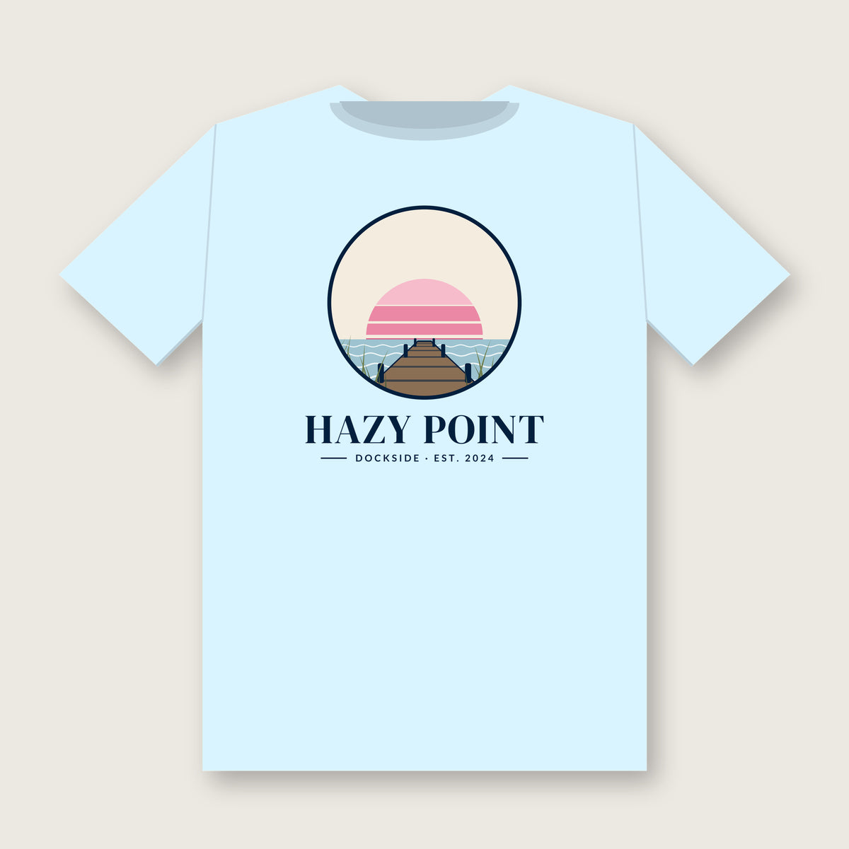 Back of the chambray-blue Hazy Point Dock Sunset Tee: a roundel of pink sunset bands, still water and weathered dock planks, with HAZY POINT and Dockside, EST. 2024 beneath