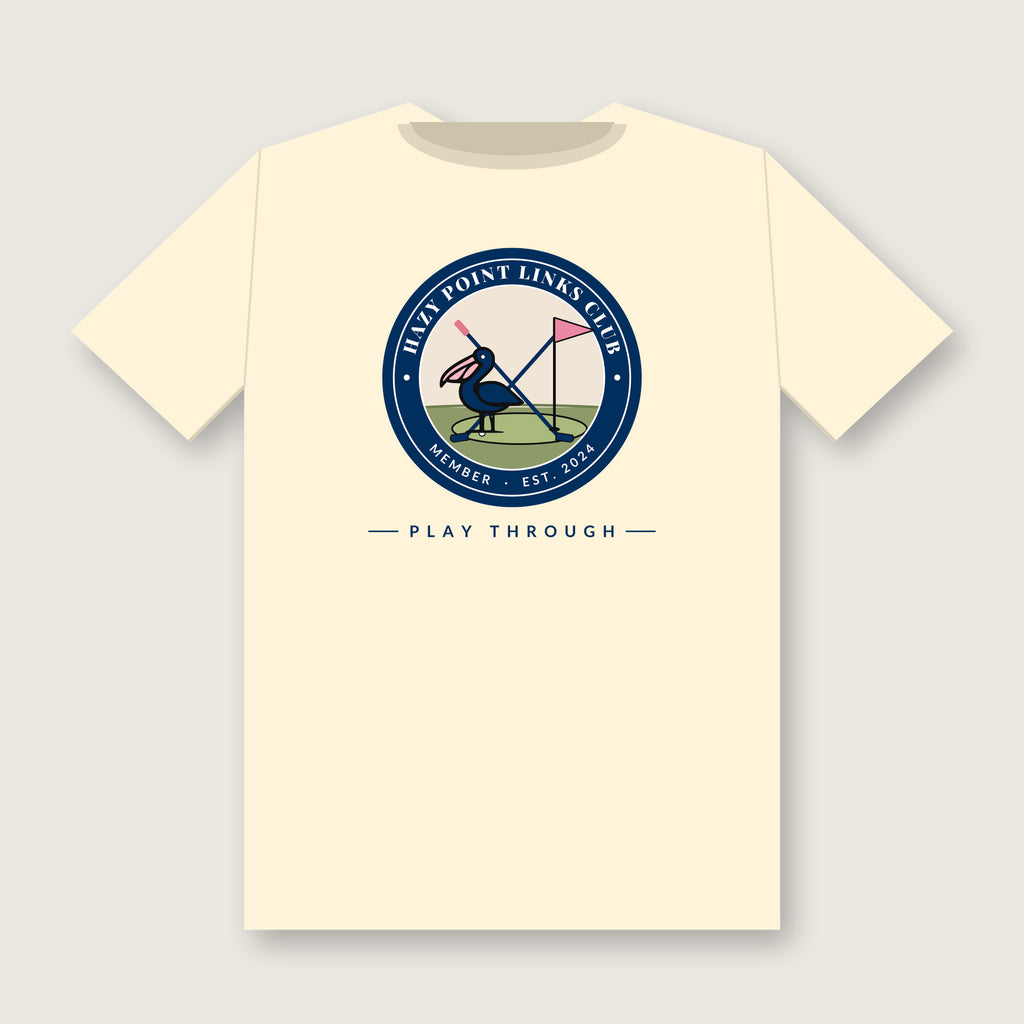Back of the ivory Hazy Point Links Club golf tee: a navy ring crest reading HAZY POINT LINKS CLUB, MEMBER, EST. 2024 around a pelican on a putting green beside a pink pin flag and crossed golf clubs, with PLAY THROUGH beneath