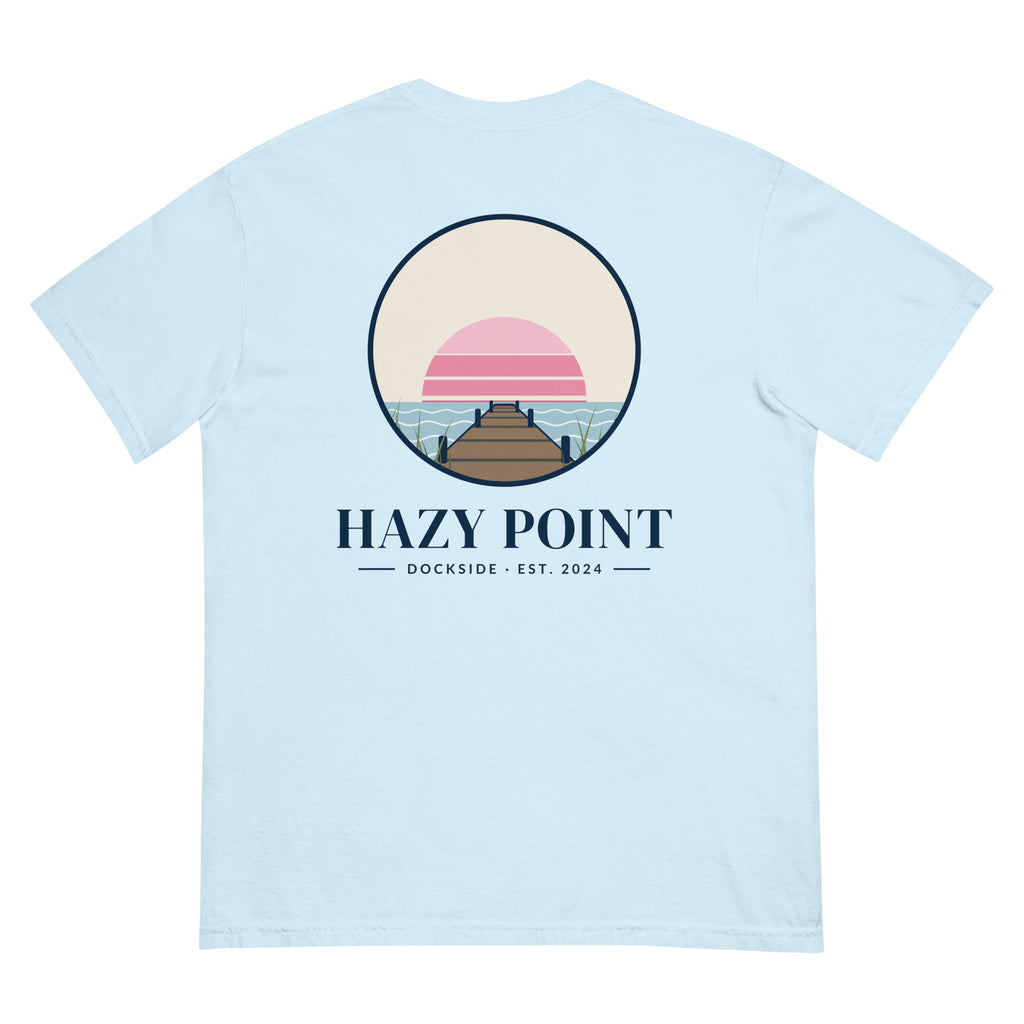 Back of the chambray-blue Hazy Point Dock Sunset Tee: a roundel of pink sunset bands, still water and weathered dock planks, with HAZY POINT and Dockside, EST. 2024 beneath