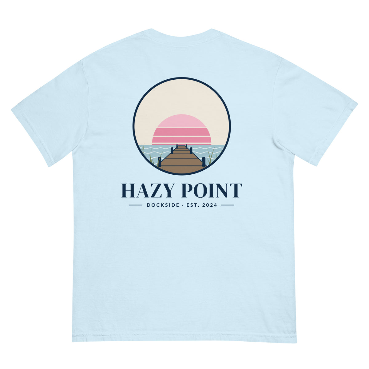 Back of the chambray-blue Hazy Point Dock Sunset Tee: a roundel of pink sunset bands, still water and weathered dock planks, with HAZY POINT and Dockside, EST. 2024 beneath